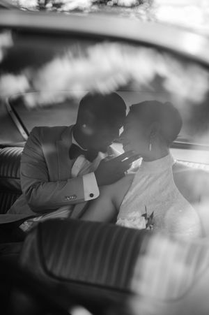 Black and white wedding photo showing couple sharing intimate moment in vintage car backseat.