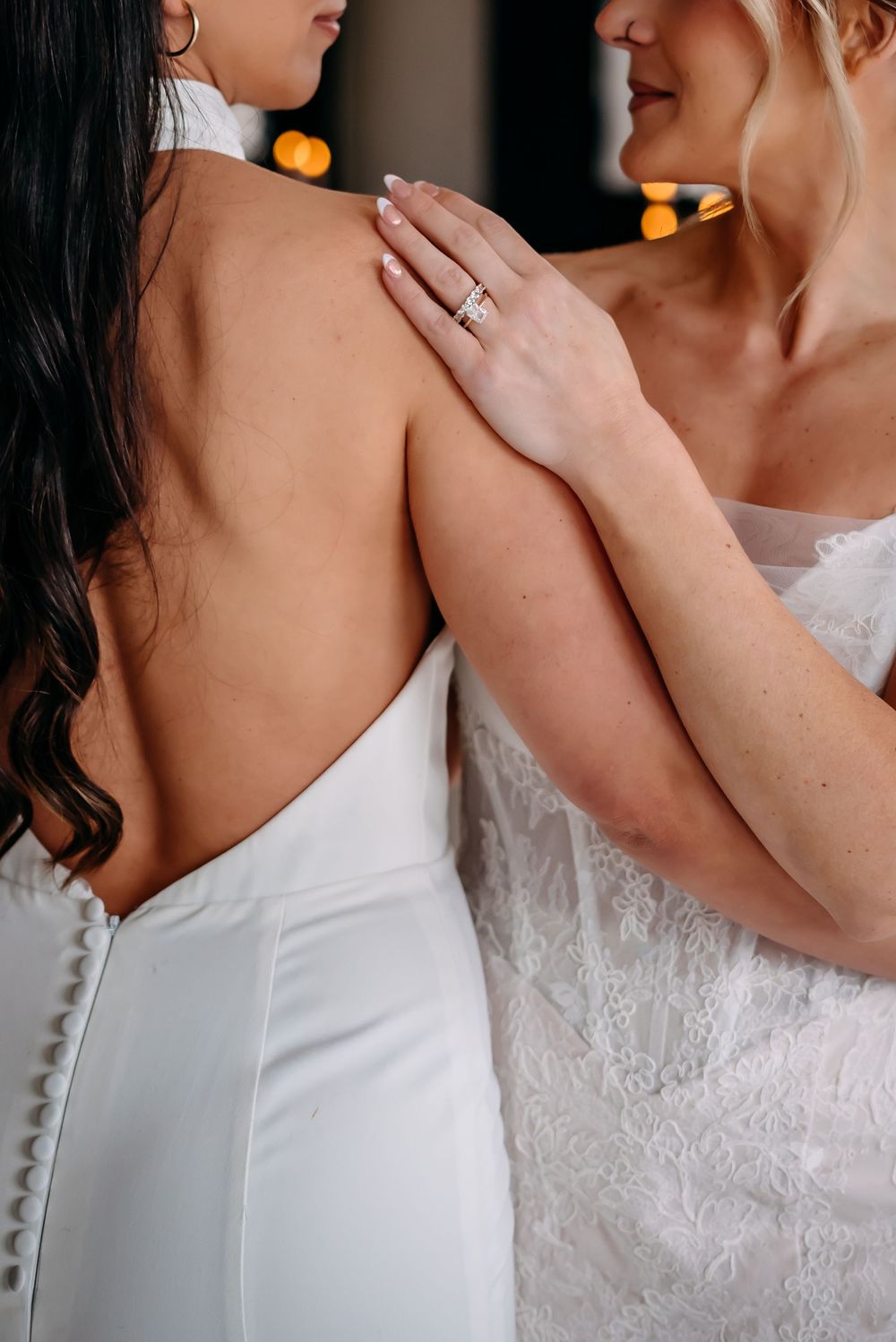 Close up detail of two women in elegant white dresses with one showing a delicate ring.