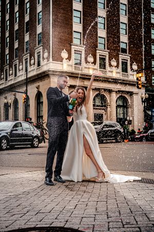 A couple celebrates with champagne on a snowy winter evening outside a historic brick building in an urban setting Grand Rapids, Michigan