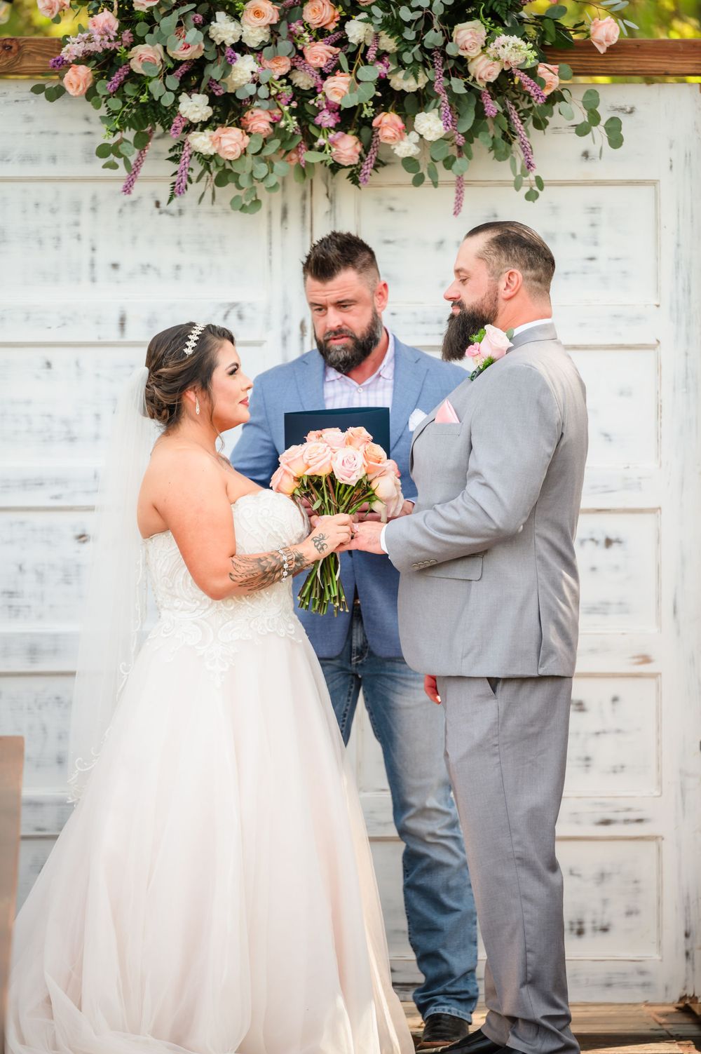 A wedding ceremony unfolds in front of a vintage white door decorated with pink floral arrangements.