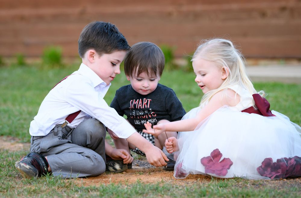 Three children in formal attire playing together on the grass during a wedding celebration.