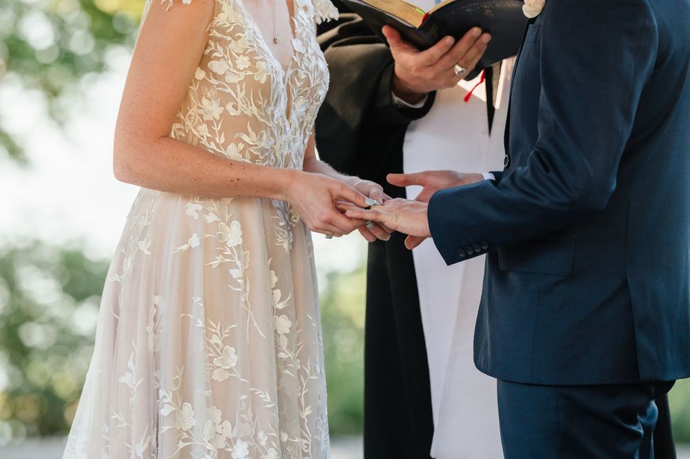 Close-up of couple exchanging rings during outdoor wedding ceremony.