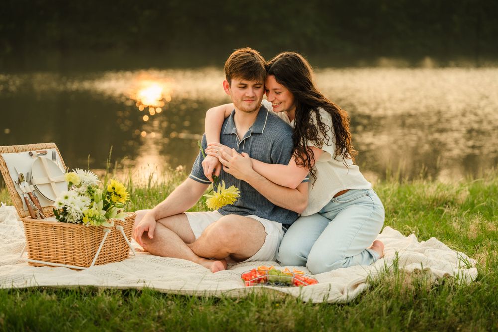 Romantic couple embraces on picnic blanket near lake during golden hour.