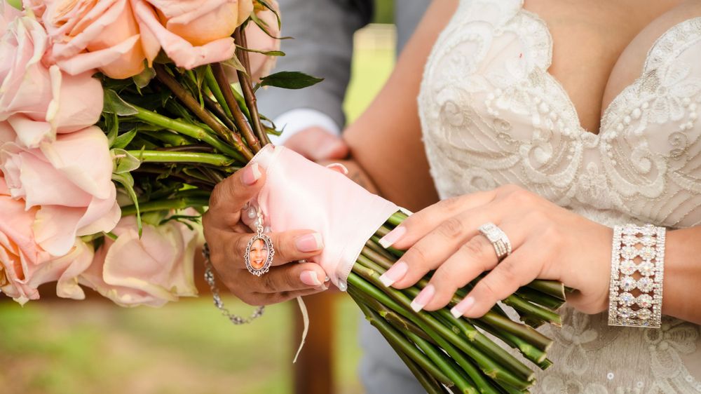 Close-up of hands holding pink rose bouquet with bracelet and ring details.