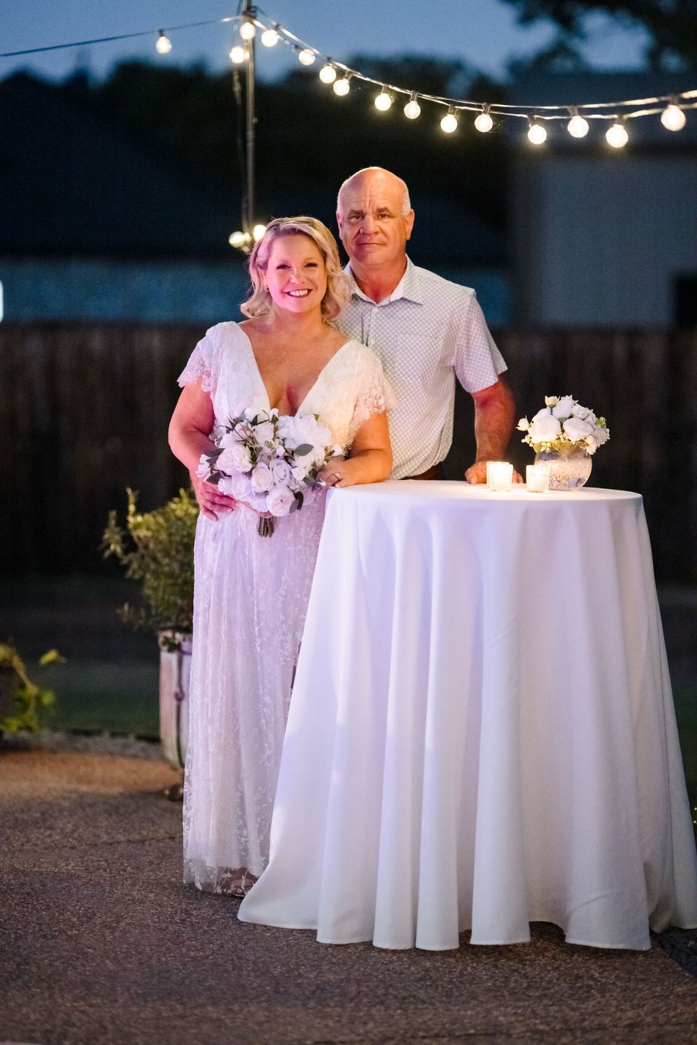 Romantic outdoor wedding reception setting with string lights and white tablecloth.