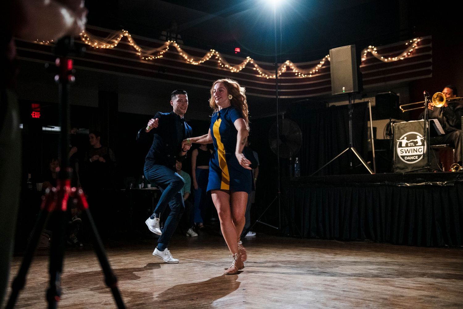 Couple dancing energetically in dimly lit venue with string lights.