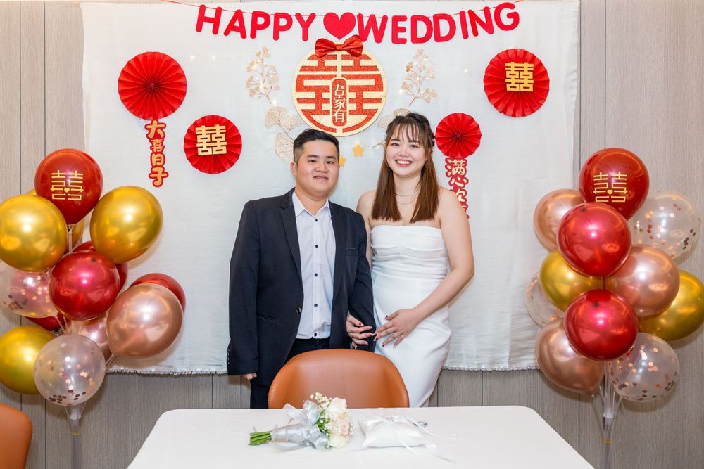 Wedding couple posing in front of decorative backdrop with red and gold balloons.