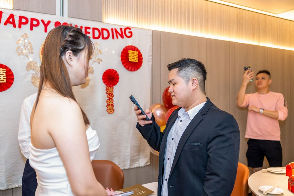 Wedding celebration with happy couple and guests in front of Chinese decorations.