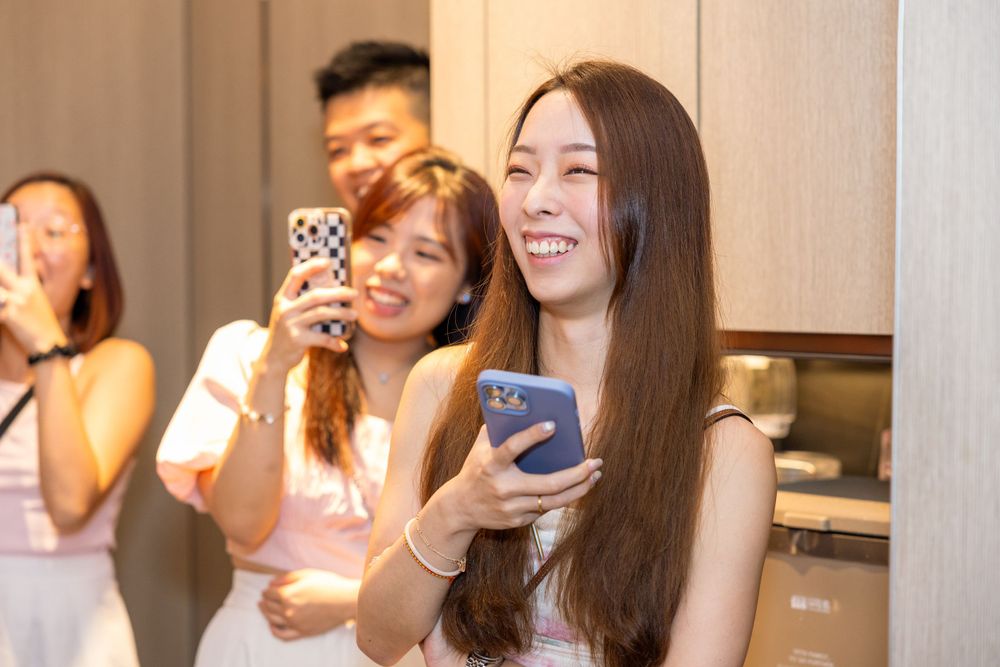 Group of friends laughing while looking at their phones at a celebration.