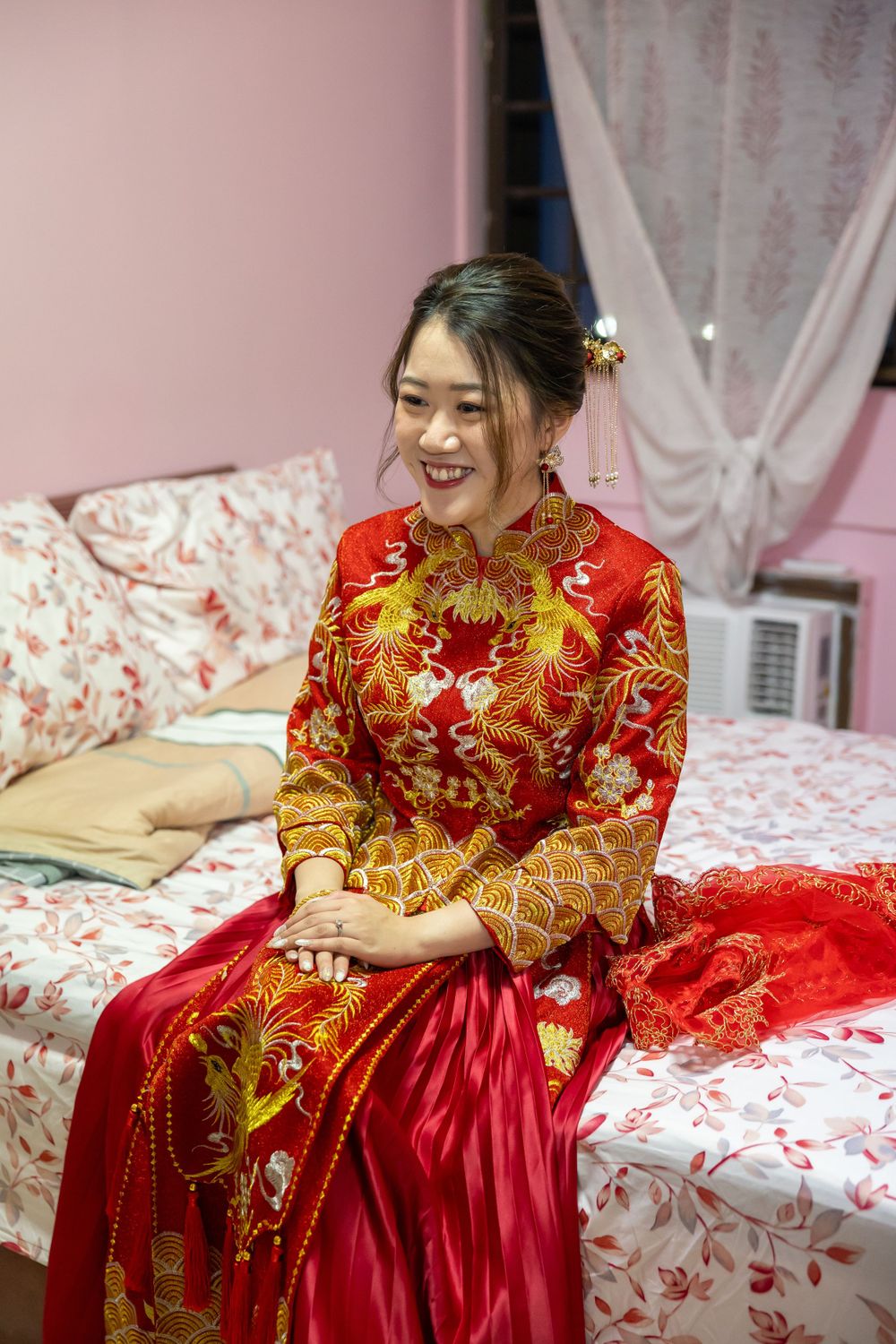 Person wearing ornate red and gold traditional Chinese wedding dress sitting on floral bedding.