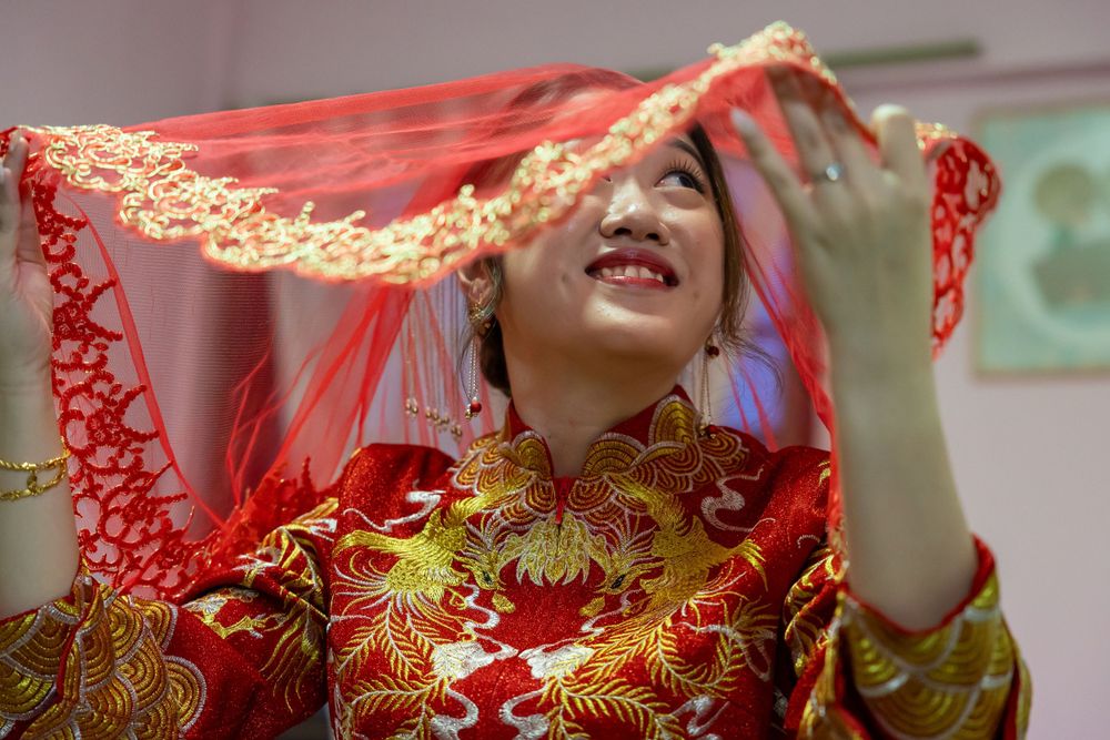 Traditional red and gold wedding veil being adjusted during Chinese ceremony preparations.
