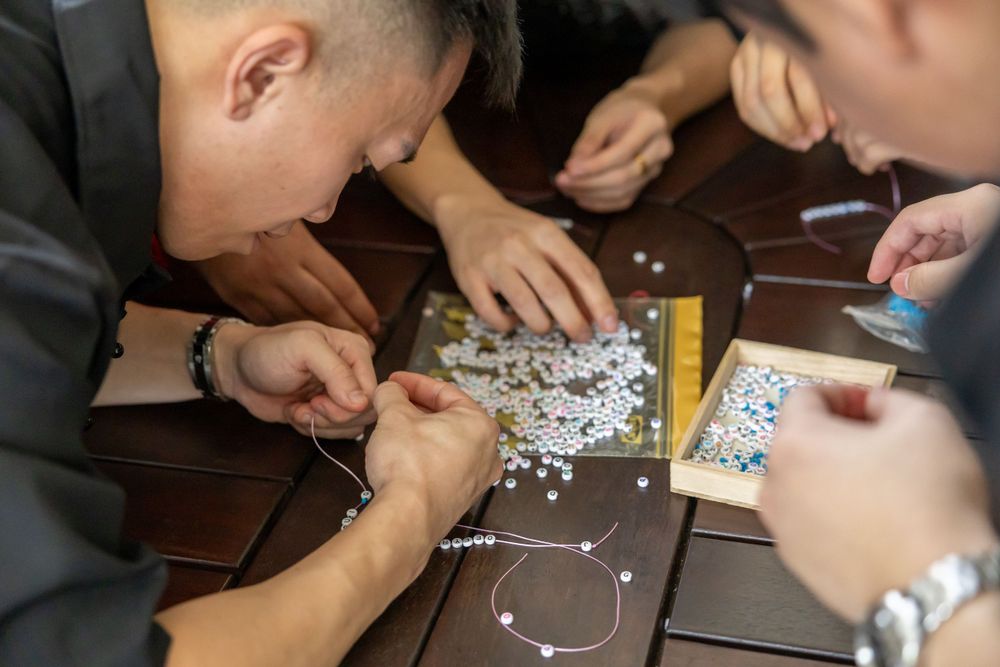 People examining and assembling jewelry pieces on a dark wooden table together.