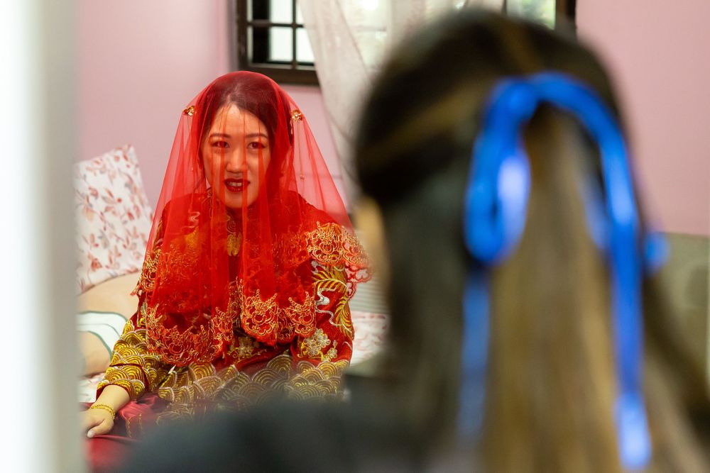 Bride wearing bright red veil with gold embroidery during traditional ceremony.