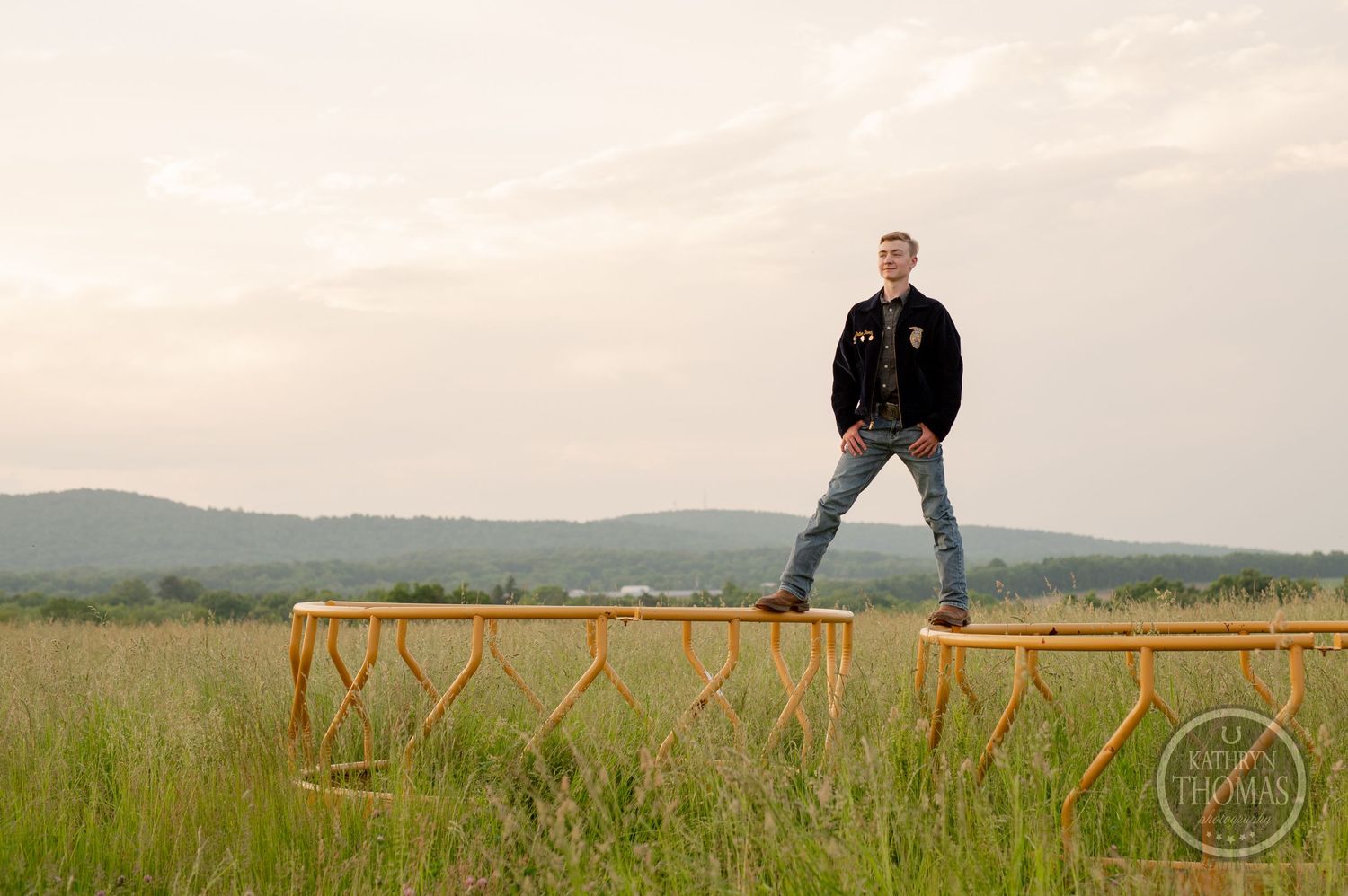 Senior photo showing student on wooden fence with rolling hills in background.