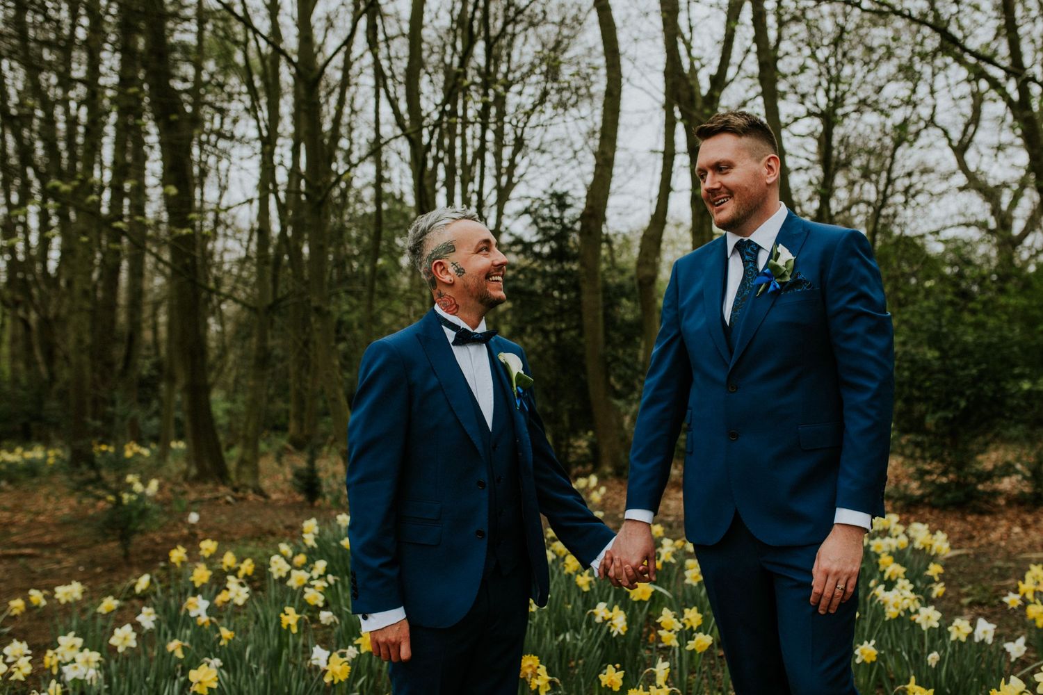 Two people in matching navy suits stand among blooming daffodils in a spring garden in Newcastle Upon Tyne.
