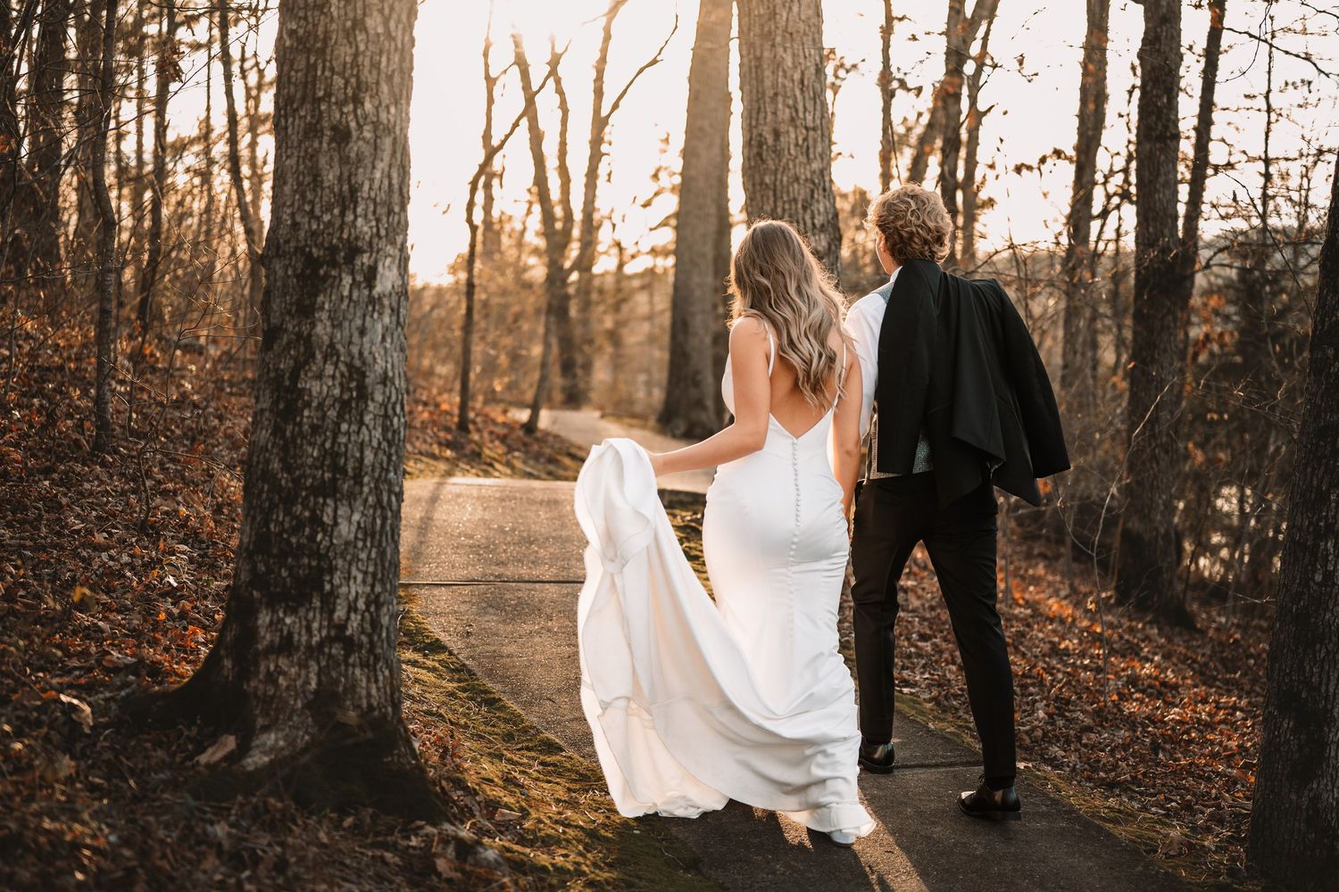 Bride in flowing white dress poses dramatically against rustic wooden barn backdrop.
