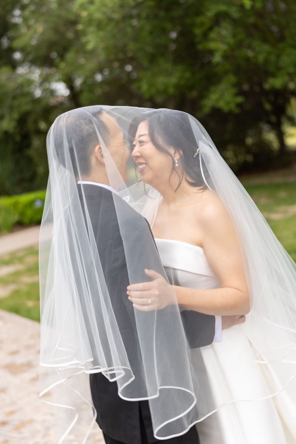 Newlywed couple sharing an intimate moment under a flowing white veil in an outdoor garden setting.