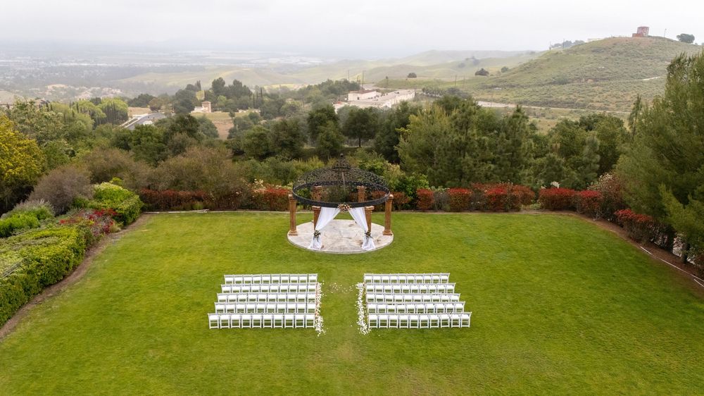 Elegant outdoor wedding ceremony setup with white chairs and gazebo on manicured lawn overlooking rolling hills.