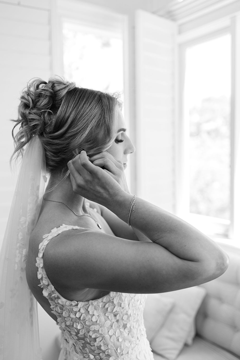 A bride wearing an elegant lace dress adjusts her earring while preparing for her wedding.