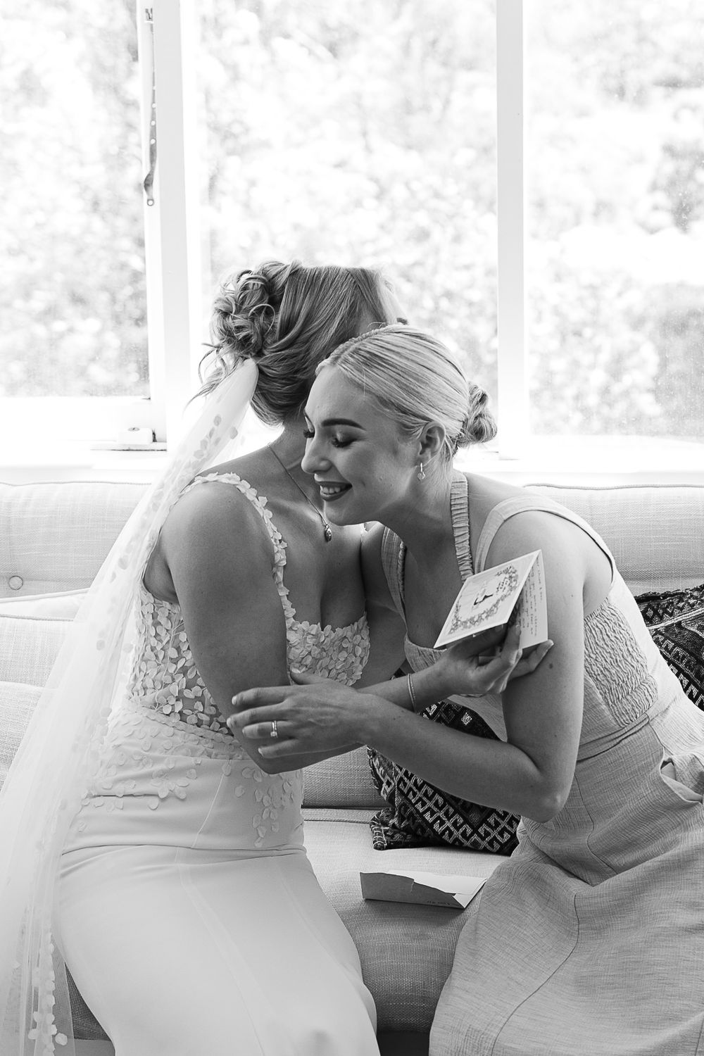 Two people wearing white dresses sitting together and sharing a joyful moment on a couch.