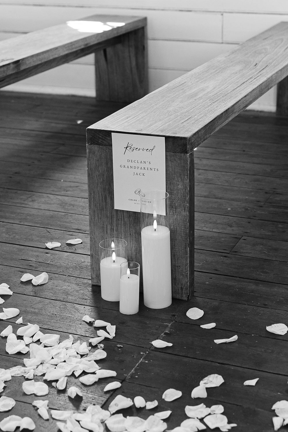 White candles and rose petals arranged on wooden benches with a reserved sign.