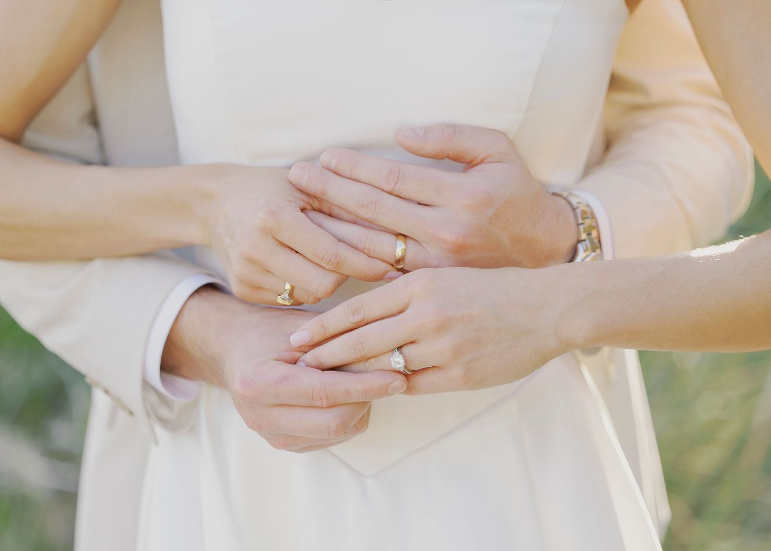 Close-up of couple's hands showing gold wedding rings and bracelet in elegant embrace.