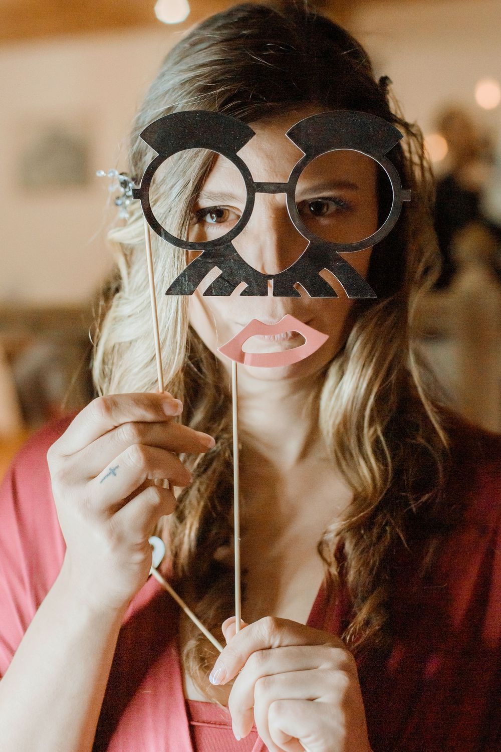 Someone poses with decorative photo booth props including oversized glasses and a mustache on a stick at a party.