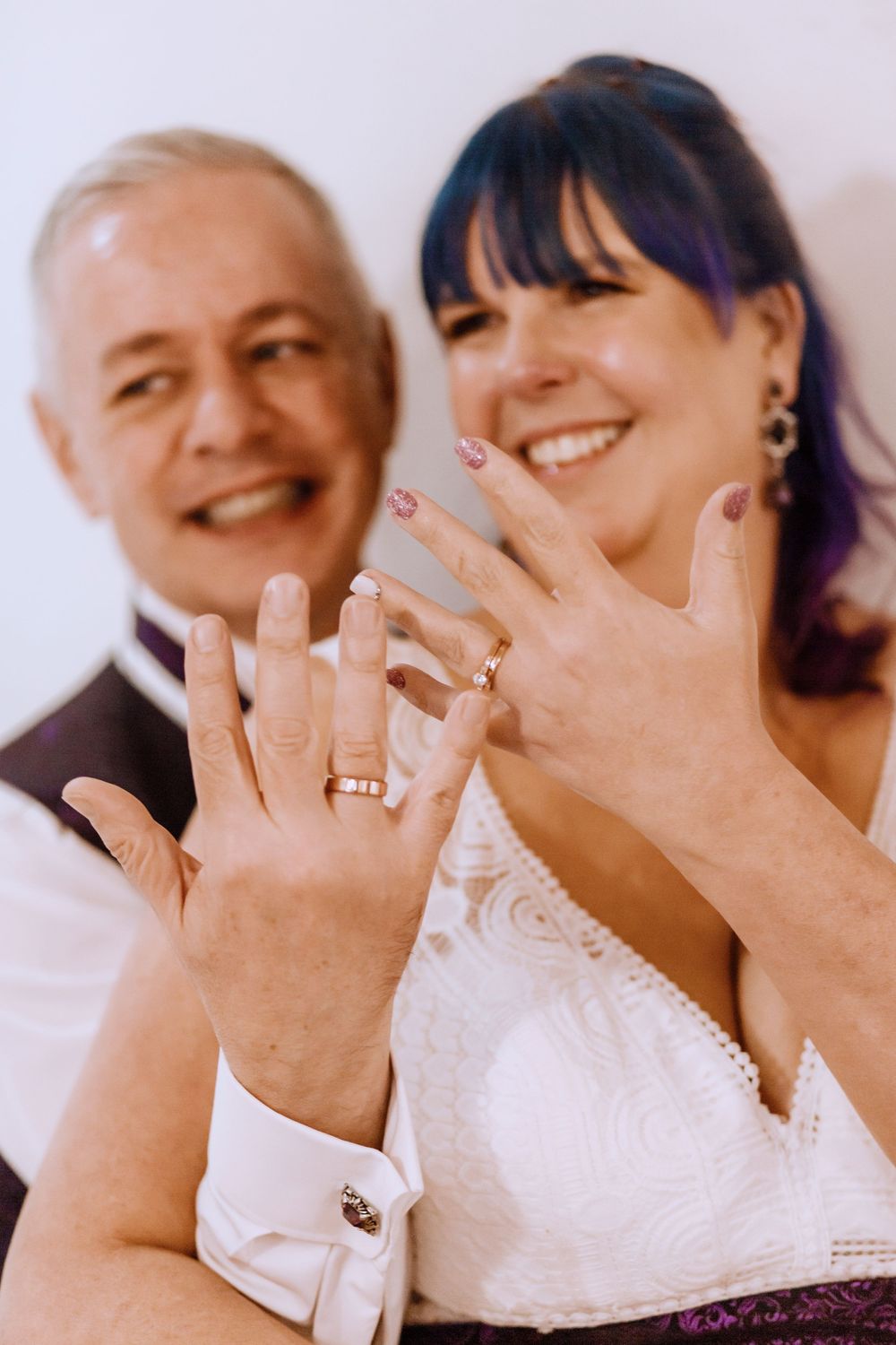 A happy couple shows off their wedding rings with joyful smiles as they celebrate their marriage.