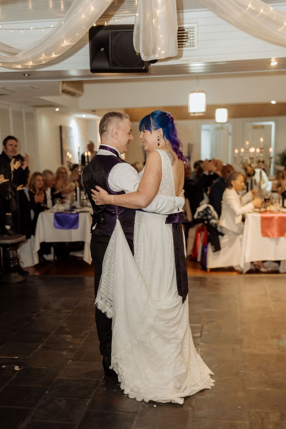 A couple shares their first dance at a wedding reception in an elegantly lit ballroom.