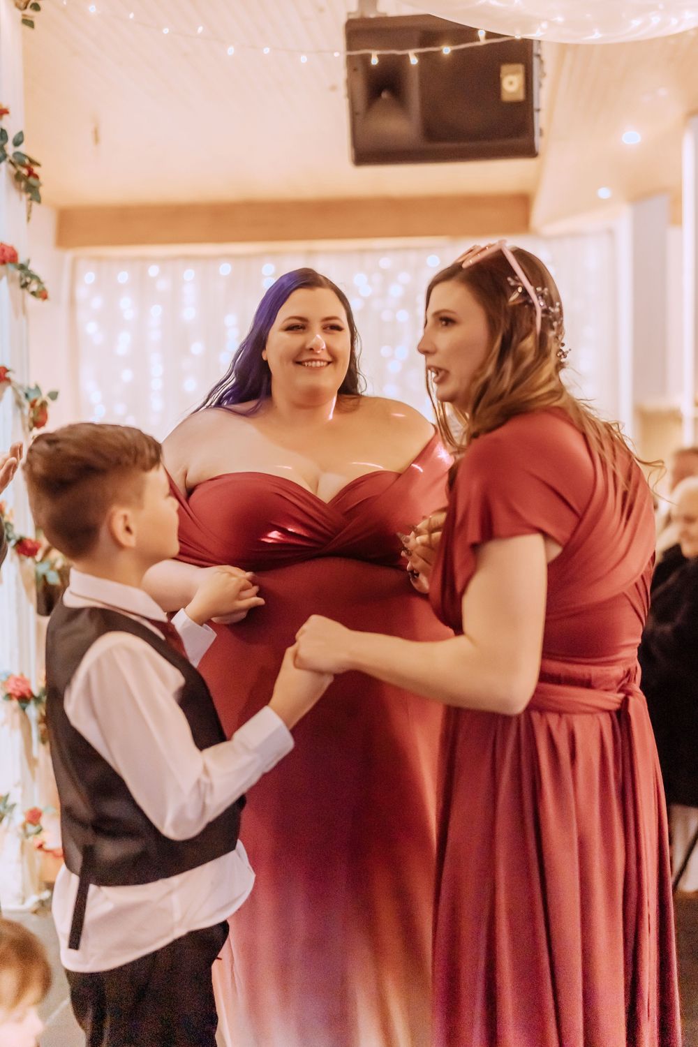 Members of a wedding party in burgundy dresses dance and interact during a reception celebration.