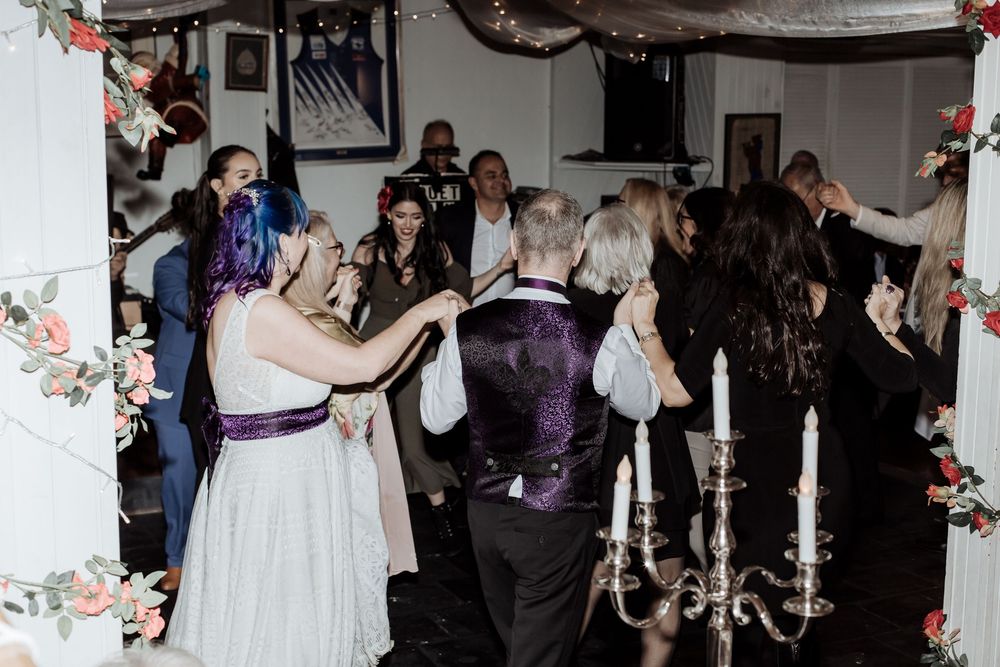 Wedding reception guests dance and celebrate on a dark dance floor decorated with floral garlands and candelabras.