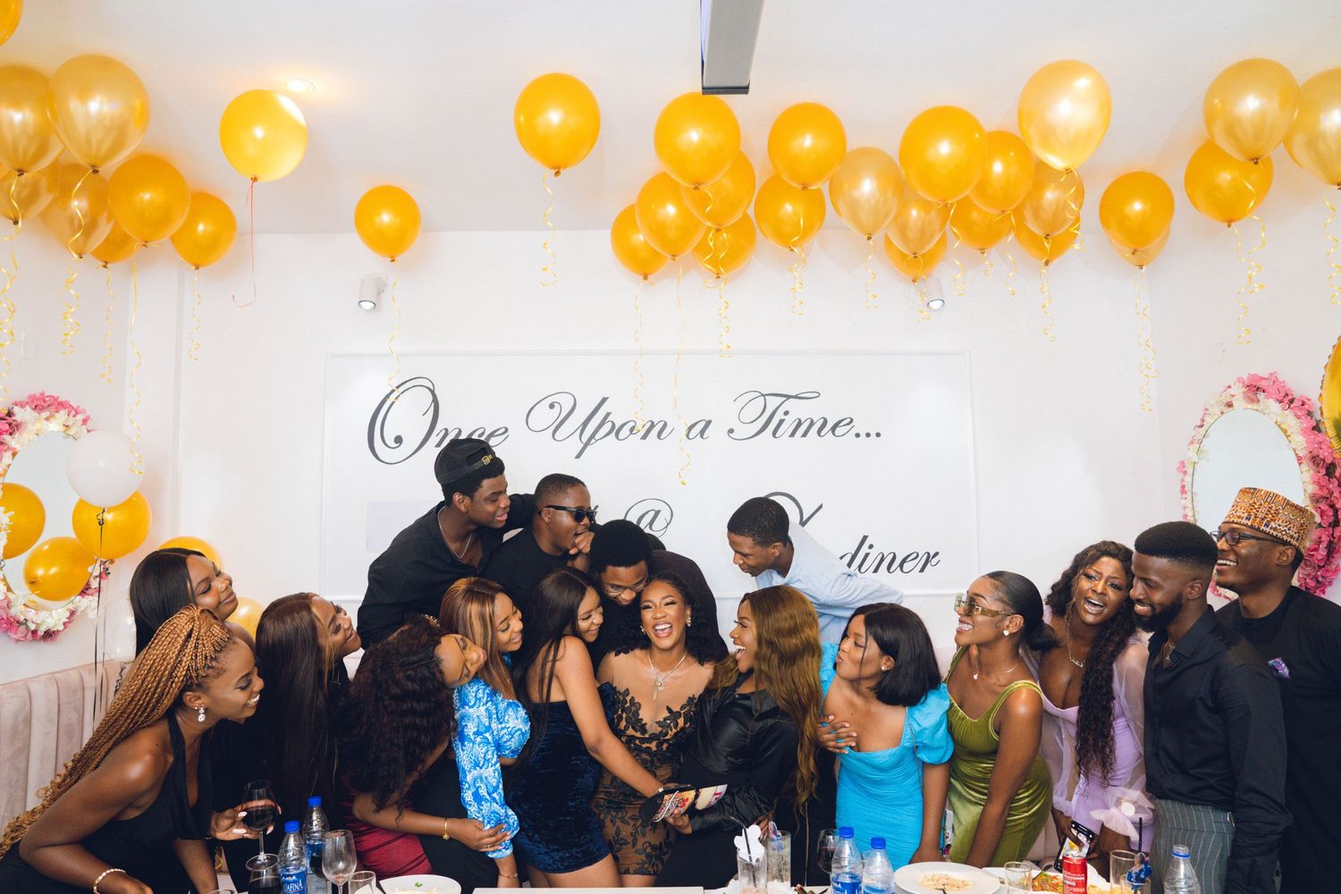 Party guests pose under yellow balloon decorations at an elegant event venue.