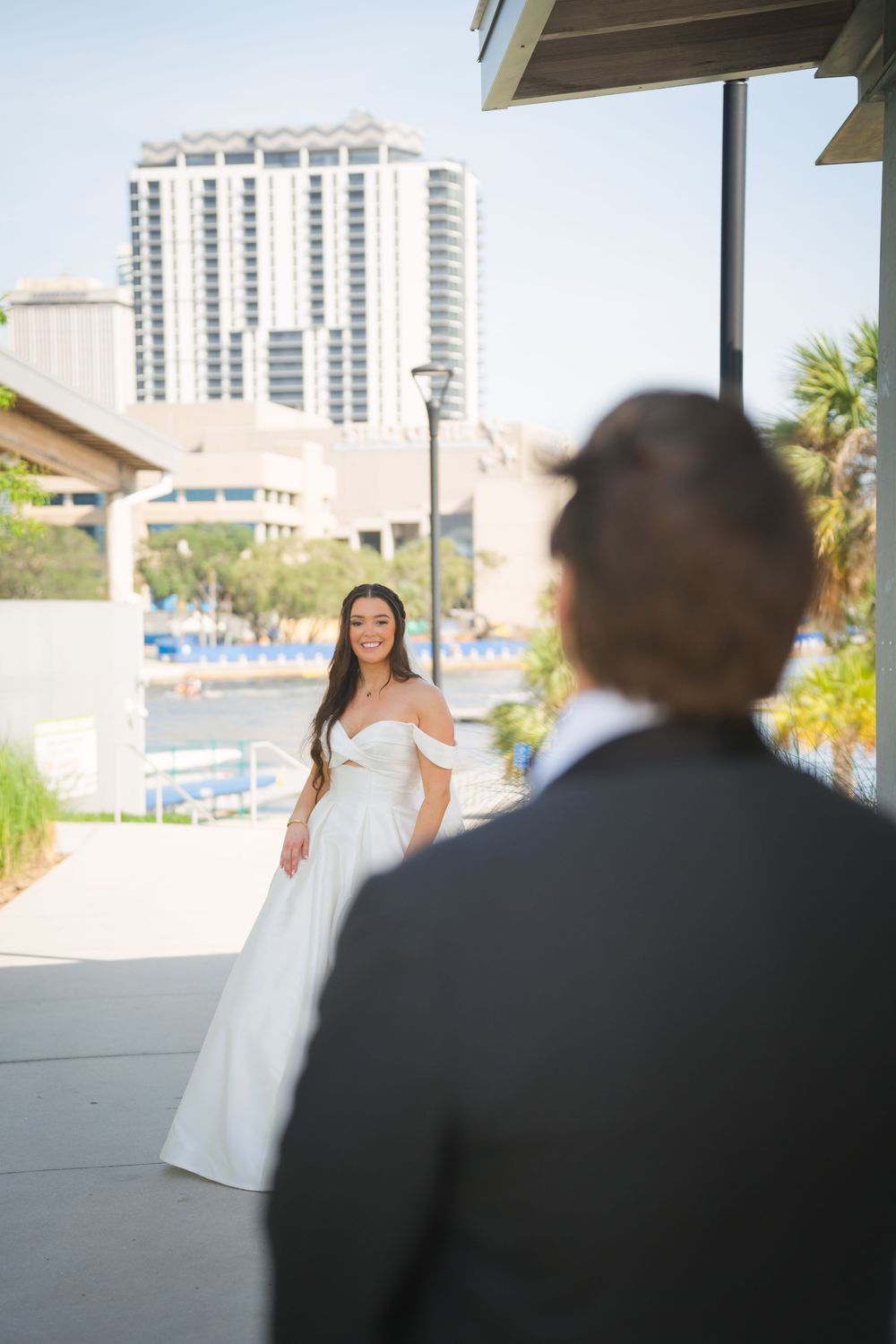 Wedding photo series showing first look moment between bride in white dress and groom at outdoor venue with city backdrop.
