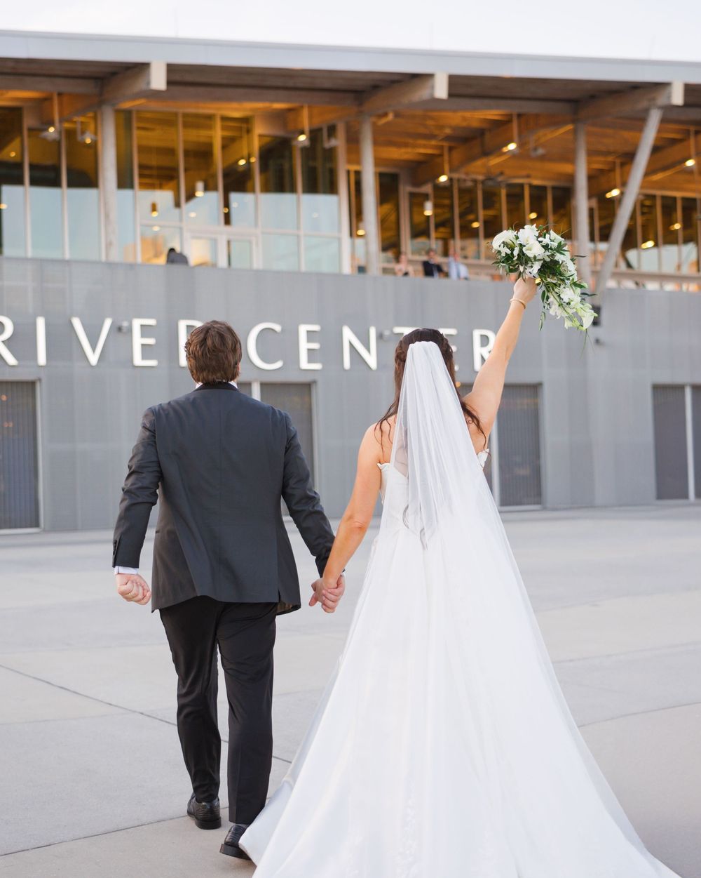 Wedding couple walks along a modern concrete patio area at an event venue.