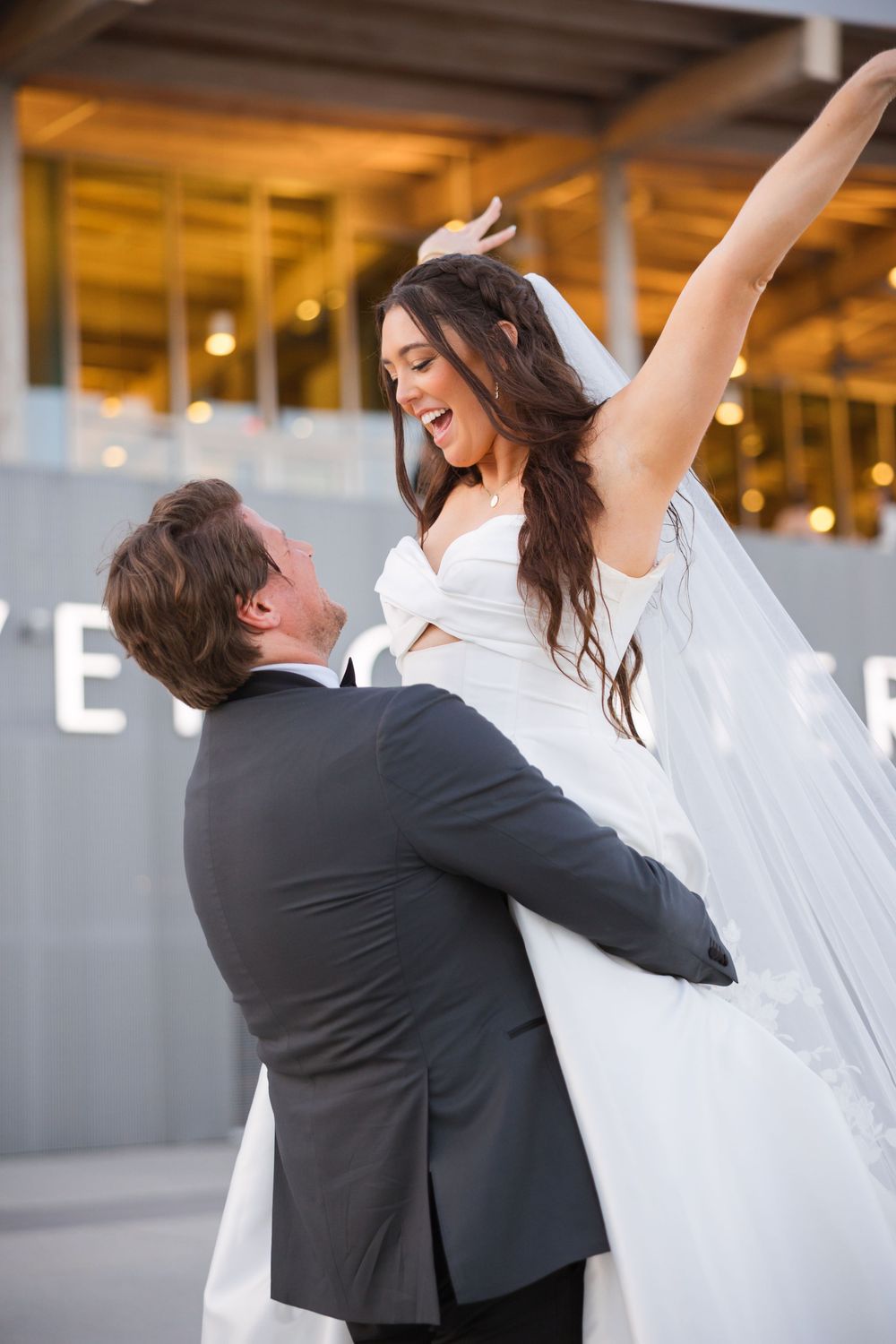 A joyful couple celebrates their wedding day, with the man lifting the bride in her white dress and veil.