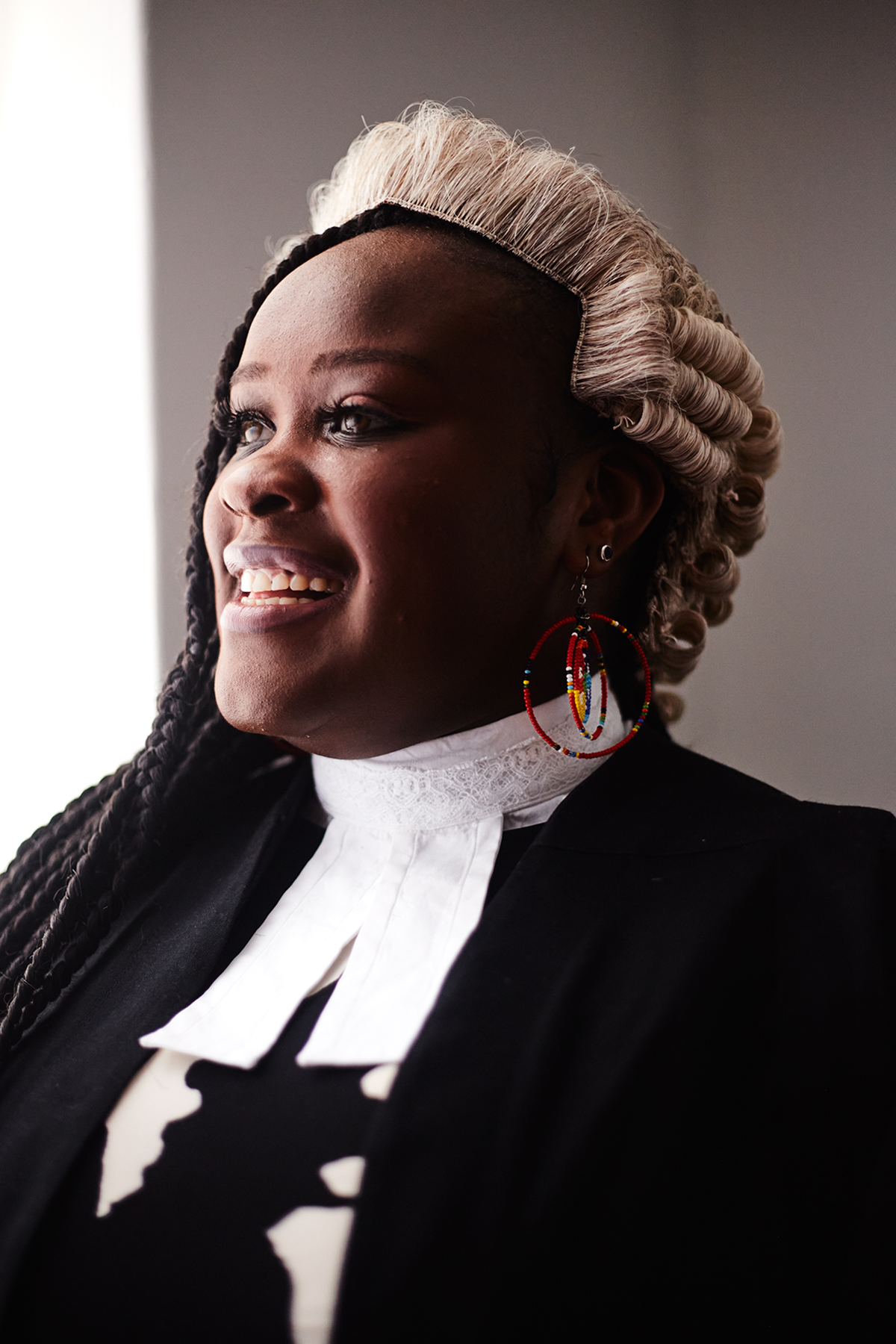 Traditional legal attire with white barrister's wig and black robe shown in dramatic studio lighting.