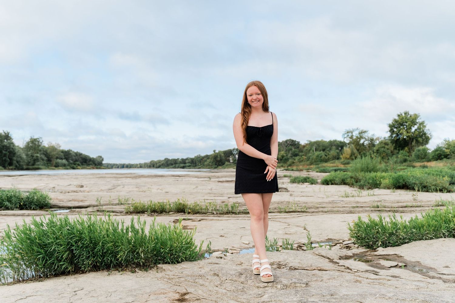 A Perrysburg High School senior in black dress poses on Maumee River at Side Cut Metropark for photo session.