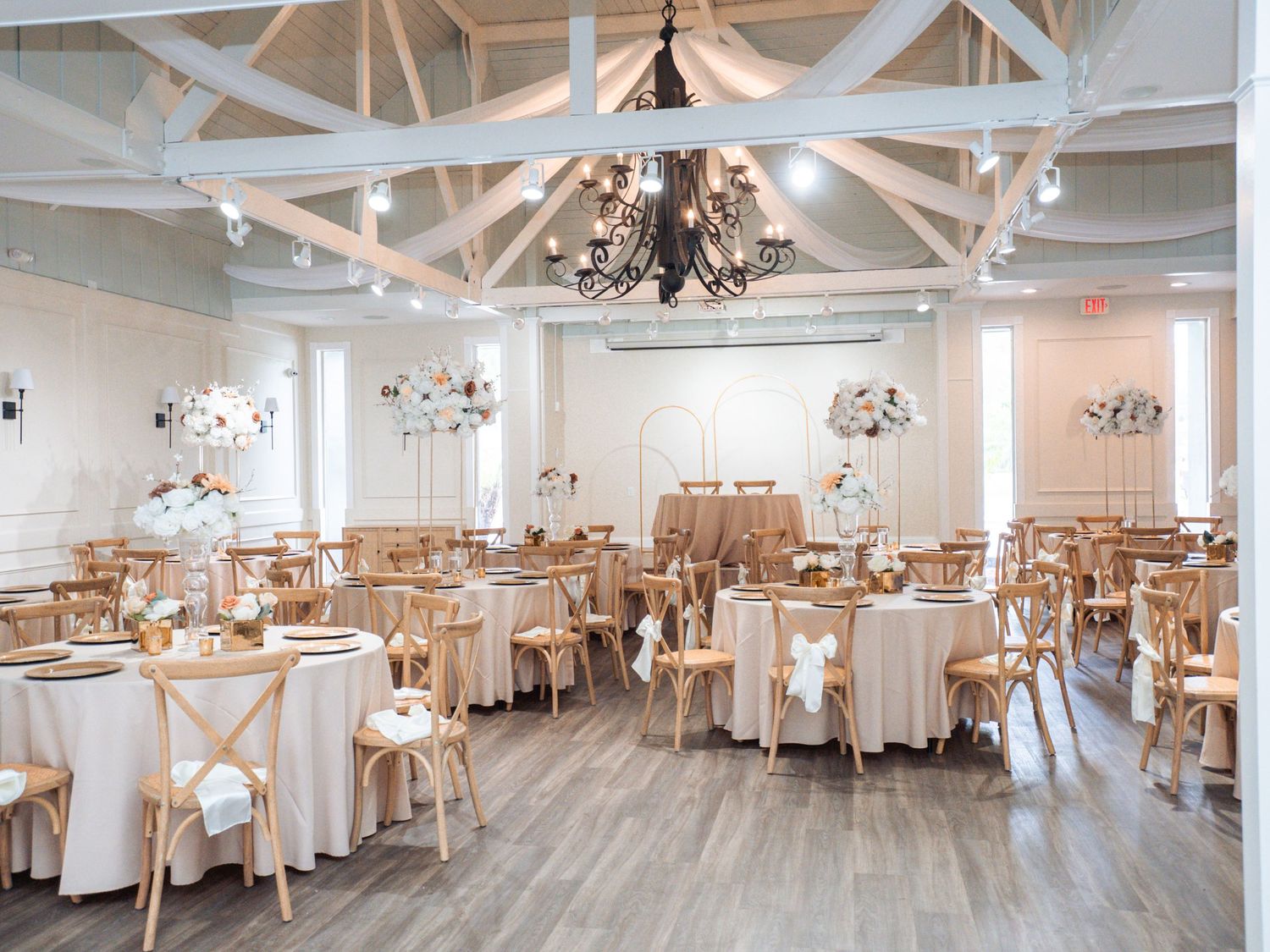 Elegant white banquet hall with chandelier lighting, exposed beams, and neutral decor for wedding receptions and events.
