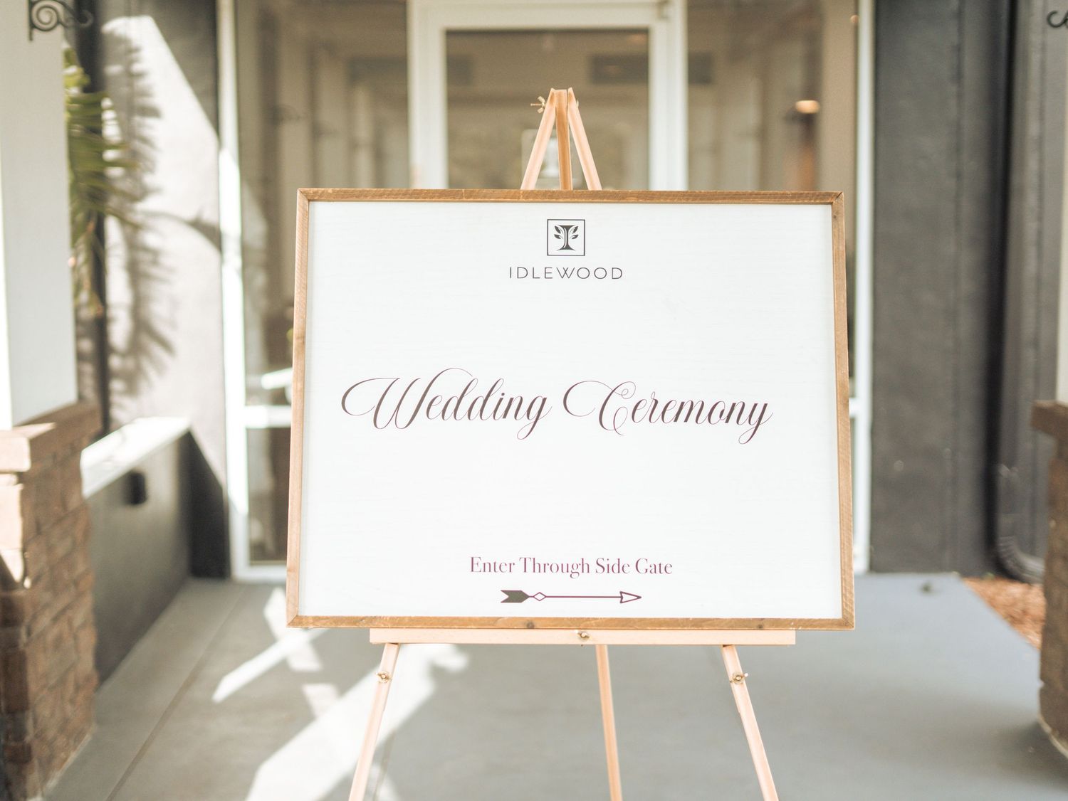 Elegant wedding ceremony sign displayed on a wooden easel with rose gold accents and calligraphy lettering.