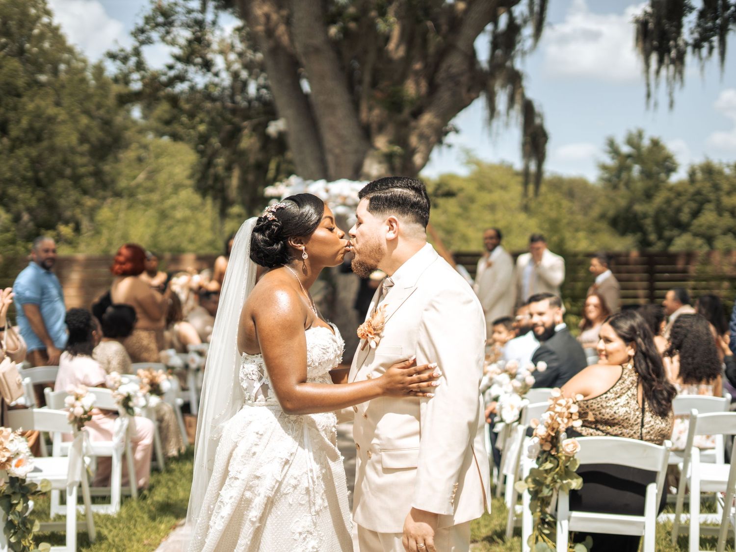 A couple shares their first kiss as newlyweds during an outdoor wedding ceremony under a Spanish moss-draped tree.