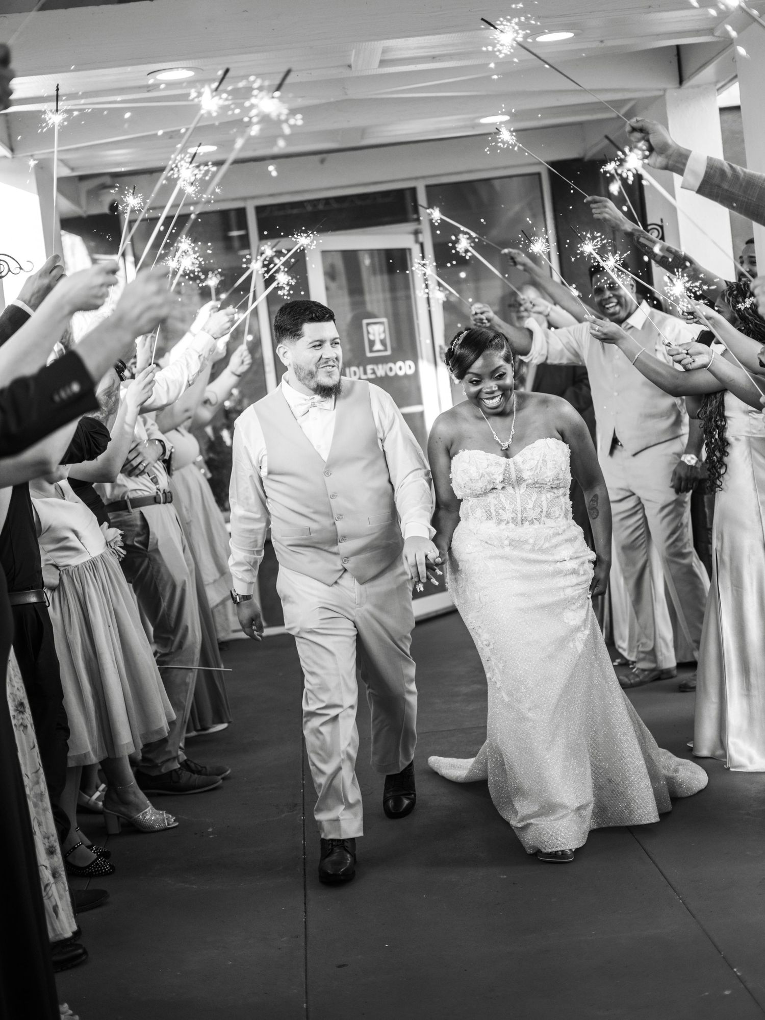 A couple walks through a sparkler exit celebration with guests holding lit sparklers during their wedding reception.
