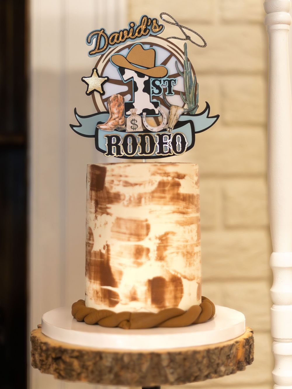 Rustic brown and white buttercream cake with custom rodeo-themed topper on wooden slice stand.