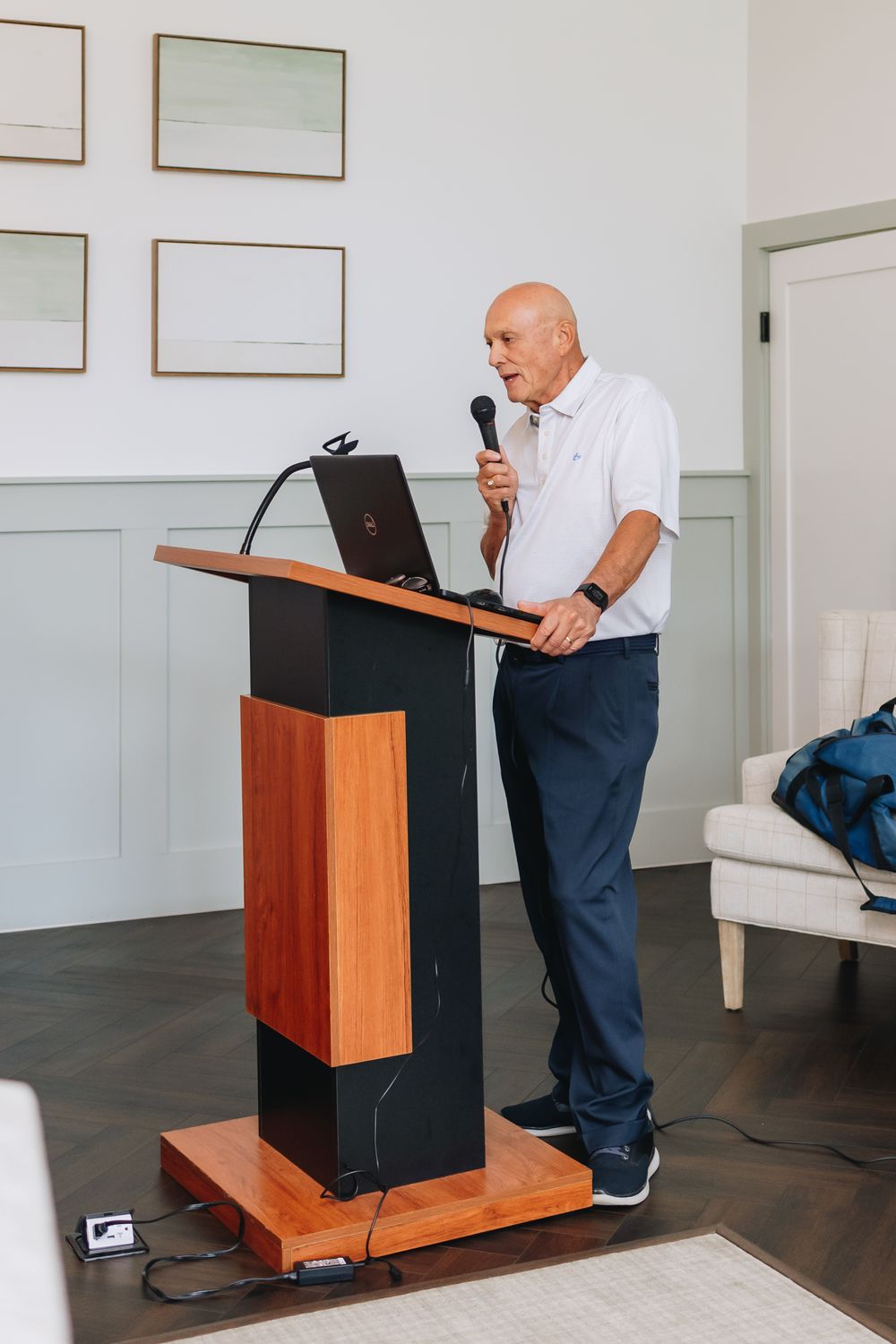 Speaker stands at wooden podium with laptop and microphone during indoor presentation.
