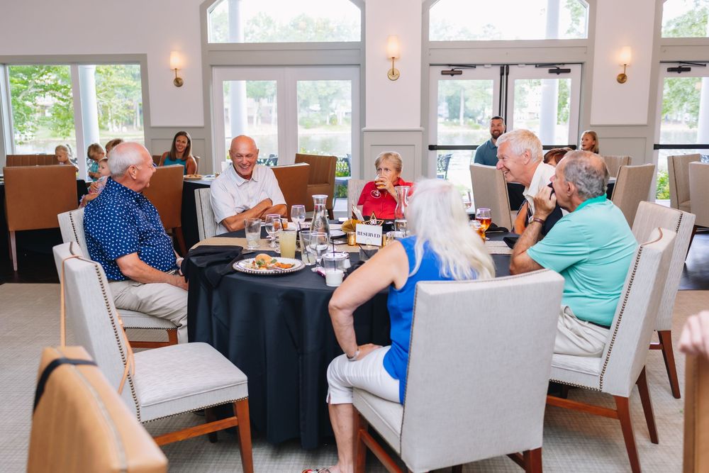Group of seniors enjoying a dining experience at a round table in an elegant restaurant with large windows.