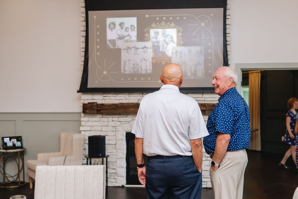 Two people stand in discussion while viewing presentation slides projected on a screen above a brick fireplace.