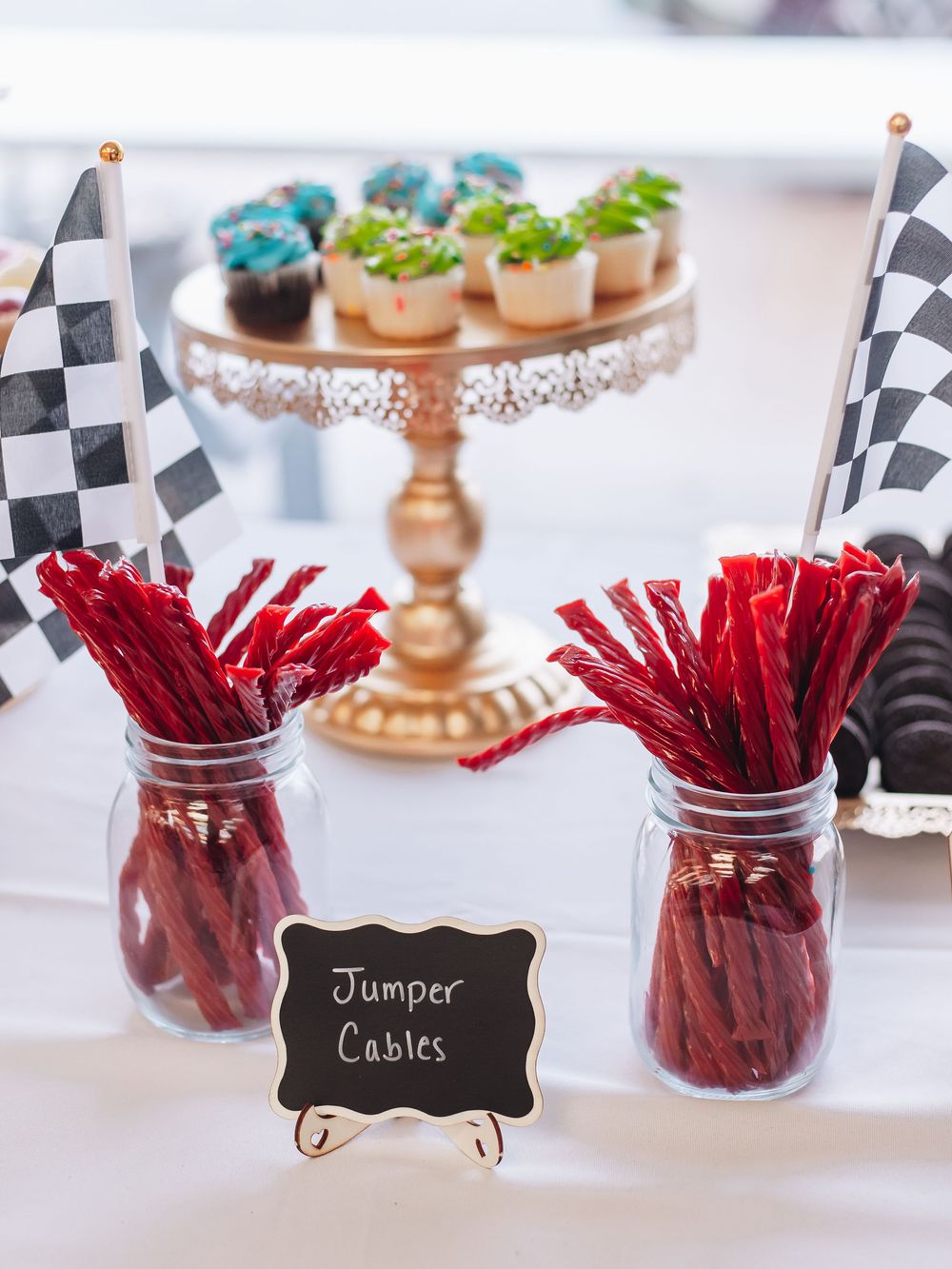 Red licorice candy displayed in mason jars with a chalkboard label and decorative cake stand in the background.