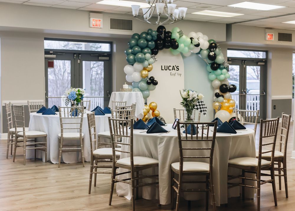 Panoramic view of an elegant event space with white tablecloths, chiavari chairs, and balloon decorations under chandeliers.