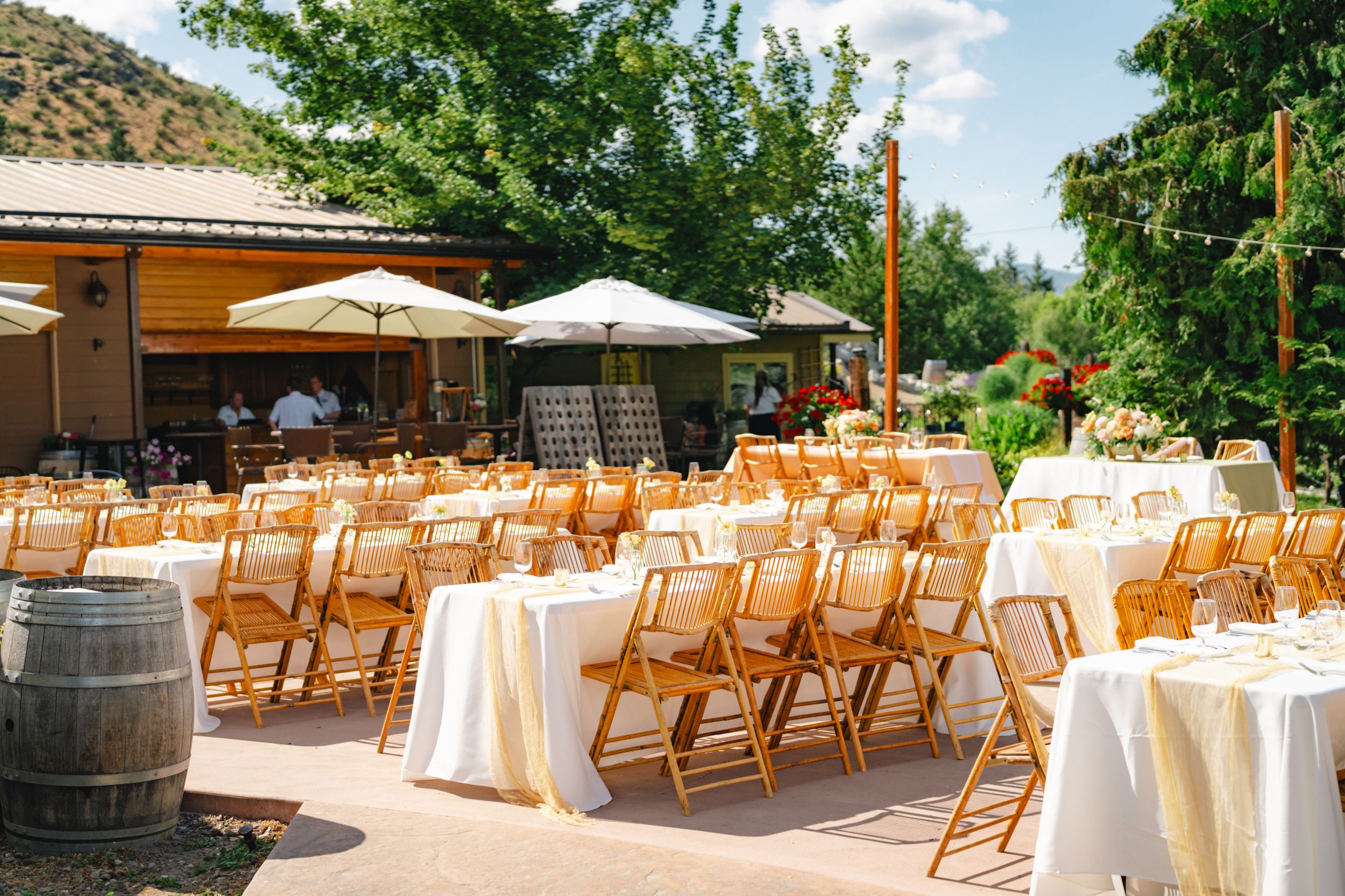 Elegant outdoor wedding reception venue with wooden chairs and round tables set up beneath white umbrellas.
