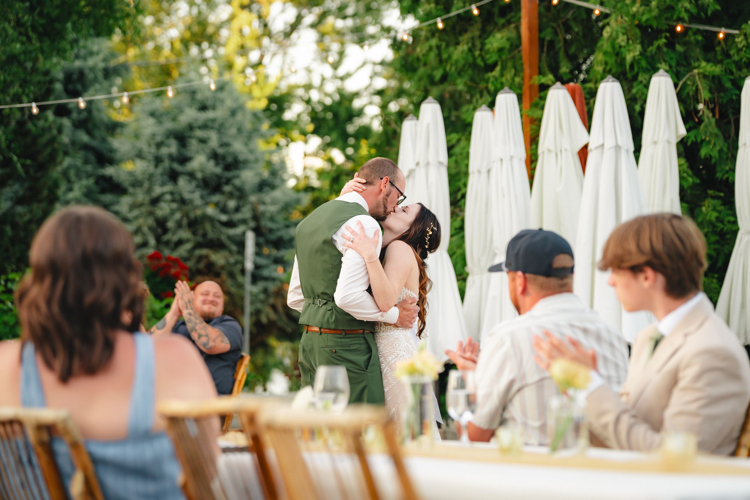 People gathered at an outdoor garden party with string lights and a white picket fence in the background.