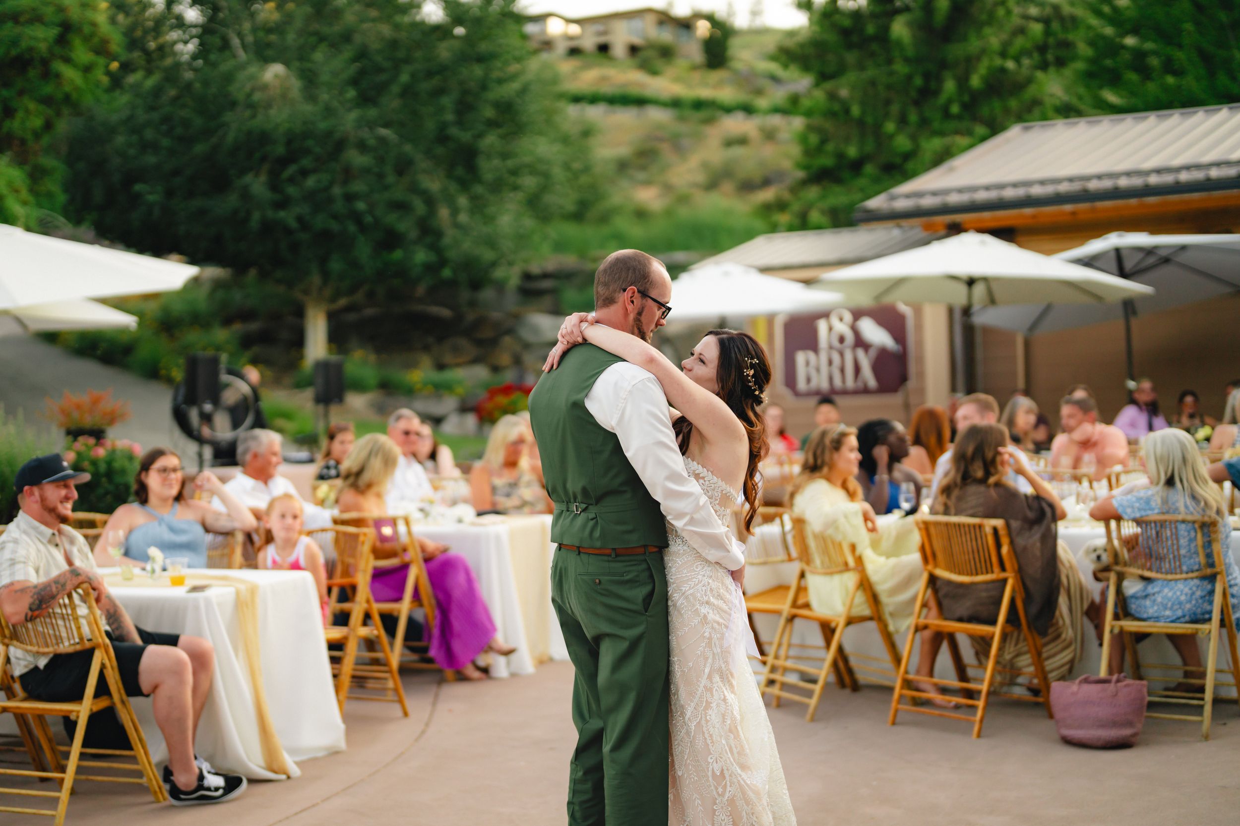 Outdoor wedding reception with wooden folding chairs and tents set up in a garden setting at sunset.